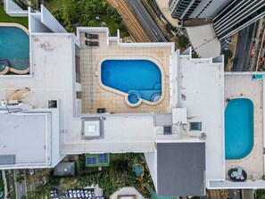 An aerial view of a rooftop with two swimming pools, a covered area, and surrounding greenery. - Ocean Vista Penthouse - Private Pool & BBQ, WiFi (Surfers Paradise)