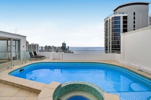 A rooftop swimming pool with a city view, a glass door entrance, and a curved building structure. - Ocean Vista Penthouse - Private Pool & BBQ, WiFi (Surfers Paradise)
