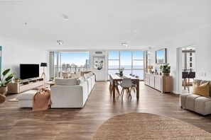 A spacious living area with a large TV, sofa, dining table, and kitchen area. - Ocean Vista Penthouse - Private Pool & BBQ, WiFi (Surfers Paradise)
