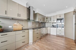 A modern kitchen with light-colored cabinets, a central island, and a built-in oven. - Ocean Vista Penthouse - Private Pool & BBQ, WiFi (Surfers Paradise)