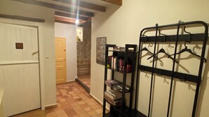 A hallway with a tiled floor, a coat rack, and a door leading to another room.