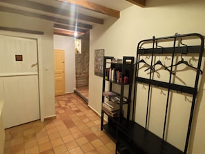 Un couloir avec un sol carrelé, un porte-manteau et une porte donnant sur une autre pièce.
