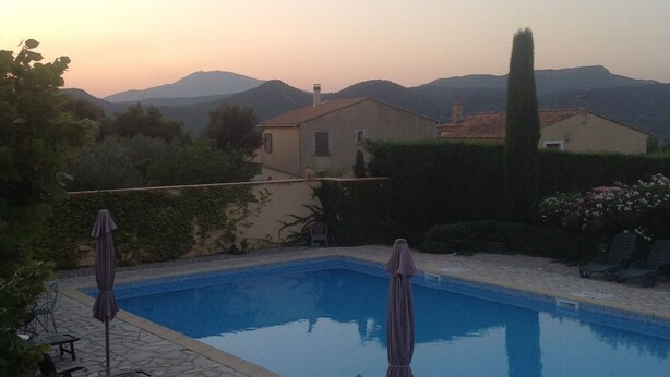 A swimming pool with lounge chairs and umbrellas, surrounded by greenery and a view of distant mountains.