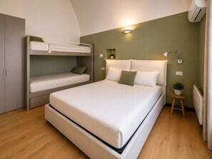 A room with a bunk bed, a single bed, a small table with a plant, and a wall-mounted lamp.