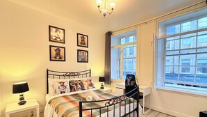 Een slaapkamer met een bed, nachtkastjes, een bureau, een stoel, een raam en wanddecoratie.