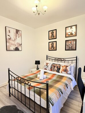Ein Schlafzimmer mit einem Metallbettgestell, einer Karo-Bettdecke und vier gerahmten Bildern an der Wand.
