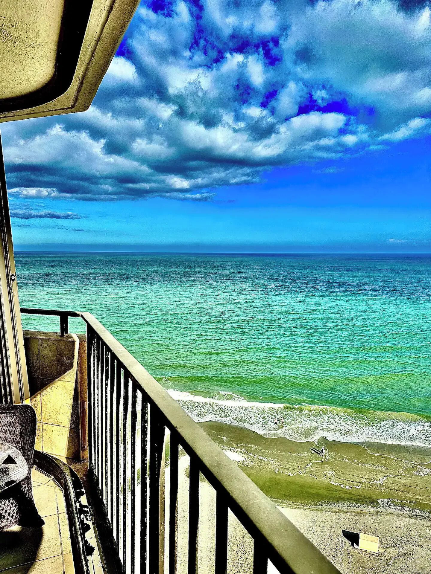 A view from a balcony overlooking a beach with clear turquoise water and a cloudy sky.