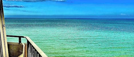 A view from a balcony overlooking a beach with clear turquoise water and a cloudy sky.