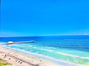 A beach with a pier extending into the ocean, clear skies, and a calm sea. - Lux Oceanfront Villa Condo on 14th Flr & Amenities (Myrtle Beach)