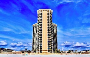 A tall, multi-story hotel with a cylindrical top, surrounded by a beach and palm trees. - Lux Oceanfront Villa Condo on 14th Flr & Amenities (Myrtle Beach)