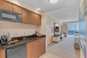 A modern kitchen with a microwave, coffee maker, and sink. There is a dining area with a table and chairs, and a view of the ocean through large windows. - Exclusive Trump Beachfront Condo (Sunny Isles Beach)