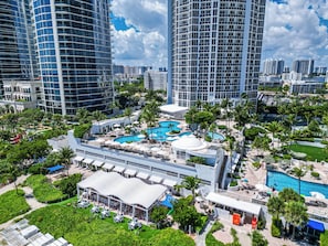 A high-rise hotel with a central pool area surrounded by palm trees and a covered outdoor seating area. - Exclusive Trump Beachfront Condo (Sunny Isles Beach)
