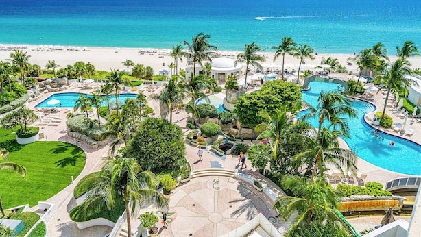 A resort with multiple swimming pools, palm trees, and a beach view. - Exclusive Trump Beachfront Condo (Sunny Isles Beach)