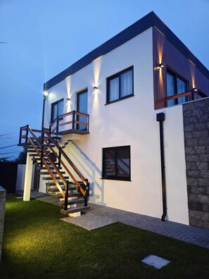 A modern two-story house with a staircase, a stone wall, and a well-lit exterior.