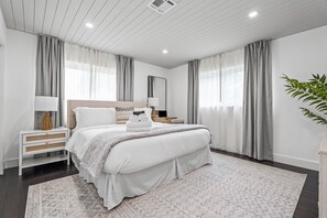 A modern hotel bedroom with a large bed, bedside tables, a mirror, and a potted plant. - Backyard Oasis, Pool, Arcade & Play, Sep Deal (Delray Beach)