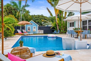 A swimming pool with lounge chairs and umbrellas, surrounded by tropical plants and a small house. - Backyard Oasis, Pool, Arcade & Play, Sep Deal (Delray Beach)