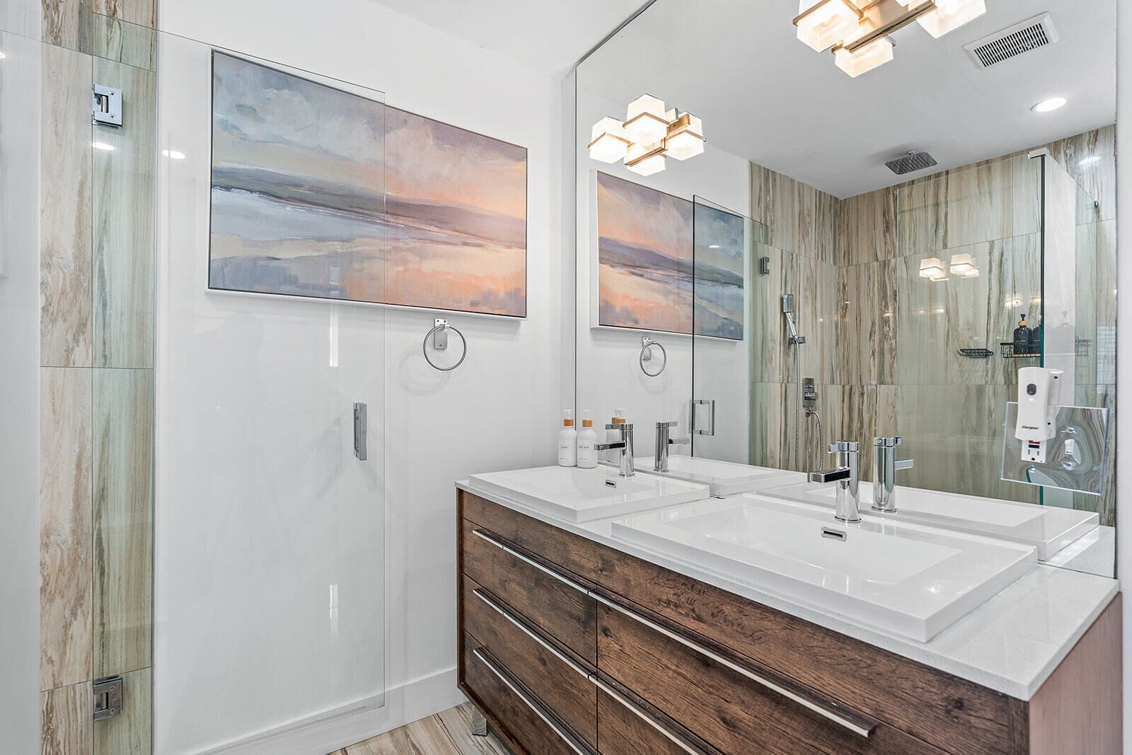 A modern bathroom with a double vanity, a glass shower enclosure, and artwork on the walls.