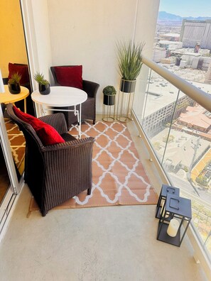 Ein Balkon mit Korbmöbeln, einem kleinen Tisch, Topfpflanzen und Blick auf die Stadtlandschaft.
