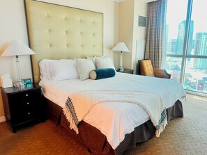 Ein Hotelzimmer mit einem großen Bett, zwei Nachttischen, einem Fenster mit Blick auf die Stadt und einem Sessel.