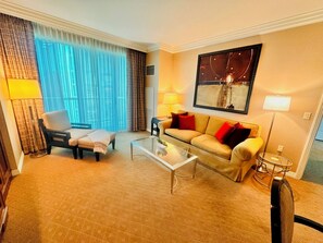 Ein Hotelzimmer mit einer Couch, einem Sessel, einem Couchtisch und einem großen Fenster mit Vorhängen.