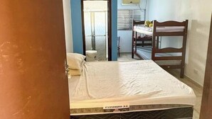 Quarto compacto com cama, escrivaninha, cadeira, janela e porta.