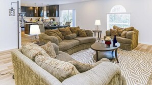 Ein modernes Wohnzimmer mit einer Eckcouch, einem runden Couchtisch und einem Essbereich mit dunklen Holzschränken.