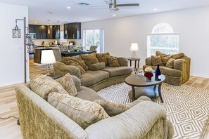 A modern living room with a sectional sofa, a round coffee table, and a dining area with dark wood cabinets. - 4 BR Palmcoast (Palm Coast)