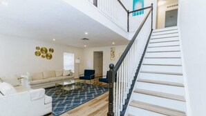 Ein geräumiges Wohnzimmer mit Treppe, einer Couch, einem Couchtisch und einem gemusterten Teppich.