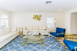 A living room with a sofa, a blue chair, a coffee table, and decorative wall art. - 4 BR Palmcoast (Palm Coast)