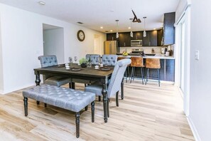 A dining area with a wooden table and upholstered chairs, a kitchen with dark cabinets and stainless steel appliances, and a light wooden floor. - 4 BR Palmcoast (Palm Coast)