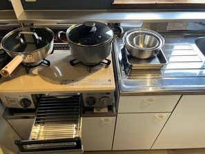 A kitchen with a stove, pots, a strainer, and a built-in oven. - Hokkaido Hideaway: Bonfire & BBQ (Toyoura)
