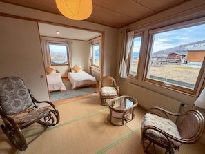 A hotel room with two beds, a sitting area with chairs, a table, and large windows offering a view of the outside. - Luxury Toya Villa: Lake Views, BBQ, Cinema & Hammock (Toyako)