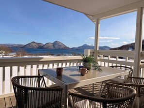 A covered outdoor seating area with a table and chairs, a potted plant, and a view of mountains and a body of water. - Luxury Toya Villa: Lake Views, BBQ, Cinema & Hammock (Toyako)