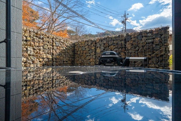 A stone wall with a grill, a clear reflective surface, and power lines in the background.