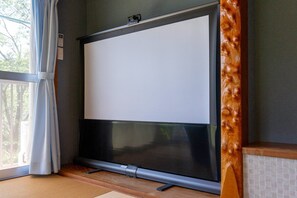 A room with a large flat-screen TV mounted on a wall, a sliding door with a curtain, and a wooden floor. - Private Palfaure Izu: Dual Cinema, Mineral Hot Spring & BBQ Area (Itō)