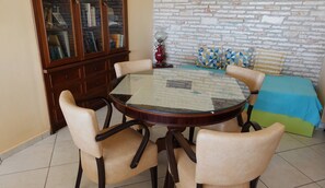 A round glass table with four chairs, a wooden cabinet, and a brick-patterned wall. - The One Bedroom Villa (Zakynthos)