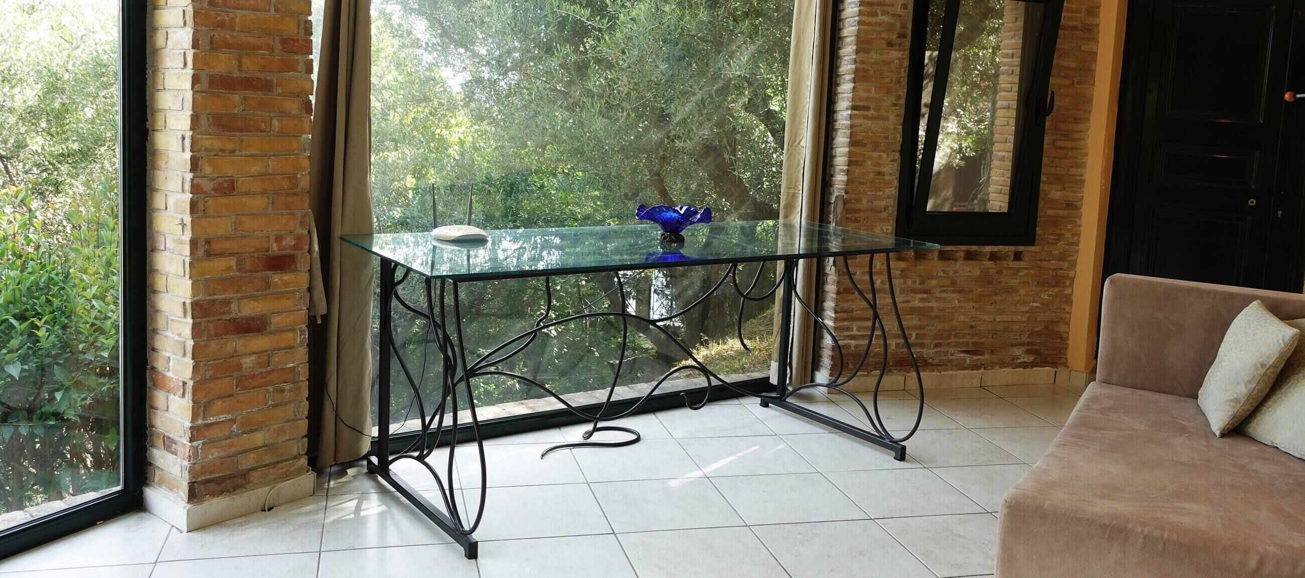 Une pièce avec une table en verre, un mur en briques, une fenêtre donnant sur un espace verdoyant et un canapé marron.
