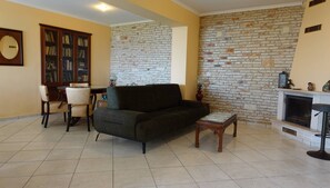 A living room with a sofa, chairs, a fireplace, a bookshelf, and a brick wall. - The One Bedroom Villa (Zakynthos)