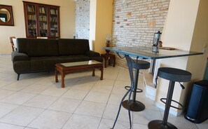 A living room with a sofa, a coffee table, a brick wall, and a small bar area with stools. - The One Bedroom Villa (Zakynthos)