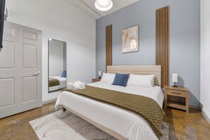 Een moderne hotelkamer met een groot bed, een spiegel, een houten hoofdbord en een nachtkastje met een lamp.