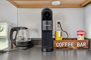 Een koffiezetapparaat, een waterkoker en een bord met daarop 'coffee bar' op een aanrecht.