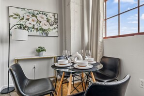 Un comedor con mesa de vidrio, sillas negras, platos blancos y un cuadro con motivos florales en la pared.