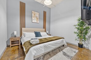 Un dormitorio moderno con cama, mesitas de noche, una obra de arte en la pared, una planta en maceta y una escalera.