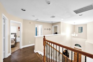 Ein mehrgeschossiges Interieur mit einer Holztreppe, einem Flur, der zu einem Schlafzimmer führt, und einem Wohnbereich mit Blick ins Freie.