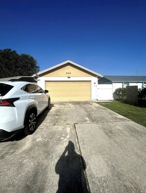 Eine Garage mit der Nummer 944 an der Wand, ein weißes Auto davor, und der Schatten einer Person auf dem Boden.