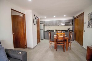 A compact kitchen with grey cabinets, a microwave, and a dining area with wooden chairs and a table. - ★ Modern Central Loft w/ Rooftop Deck, BBQ & Views (Puerto Vallarta)