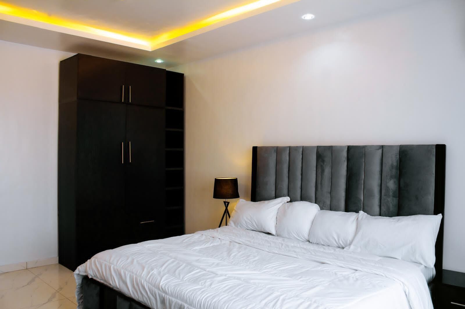 A bedroom with a bed, a wardrobe, a nightstand, and a lamp.