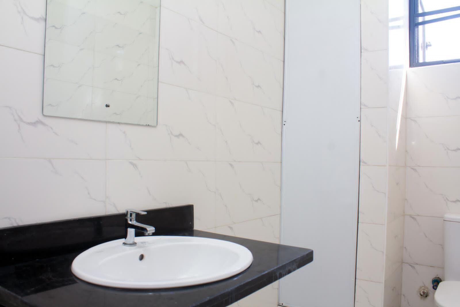 A bathroom with a white sink, black countertop, and white marble walls.