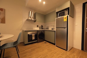 Une cuisine compacte équipée d’un four, d’un micro-ondes et d’un réfrigérateur intégrés, ainsi que d’un lave-linge et d’un coin repas avec une table et des chaises.
