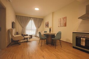 Une cuisine moderne dotée d’un four encastré, un coin repas avec une table ronde et des chaises, et un salon avec un canapé et un téléviseur.